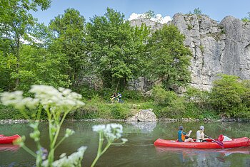 Altmühltal-Radweg bei Dollnstein Zwei rote Kanus auf einem Fluss, im Hintergrund Felsen und Bäume, im Vordergrund unscharfe Blumen.