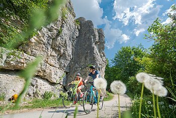 Radler auf dem Altmühltal-Radweg bei Dollnstein Zwei Radfahrer fahren auf einem Weg neben Felsen und grünen Bäumen bei blauem Himmel mit Wolken.