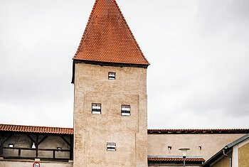 Altmühltal-Radweg (Dollnstein) Zwei Radfahrer fahren an einem historischen Stadttor mit rotem Dach und Durchfahrt vorbei.