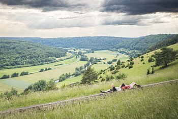 Der Altmühltaler-Panoramaweg an der langen Bank bei Obereichstätt Zwei Wanderinnen liegen auf einer langen Holzbank und schauen ins weitläufige grüne Altmühltal.